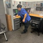 Office cleaning service being provided, lady cleaning office desk at auto dealership.