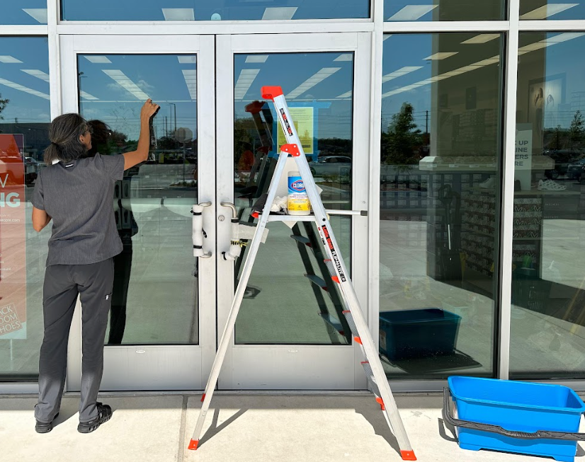 Retail cleaning service performed, woman wiping window of the store.