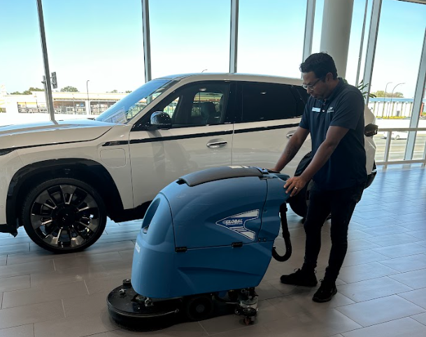 Cleaning team member pressure washing floor at auto dealership.